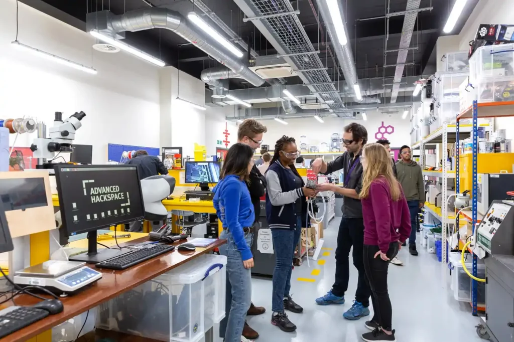 Group of people exploring a university advanced hackspace workshop with lab benches, tools and technical equipment.