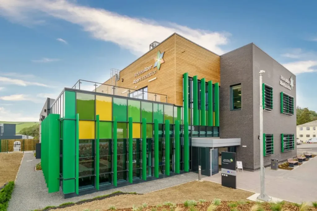 Exterior of the AberInnovation building with green glass panels, timber cladding and modern research facilities.